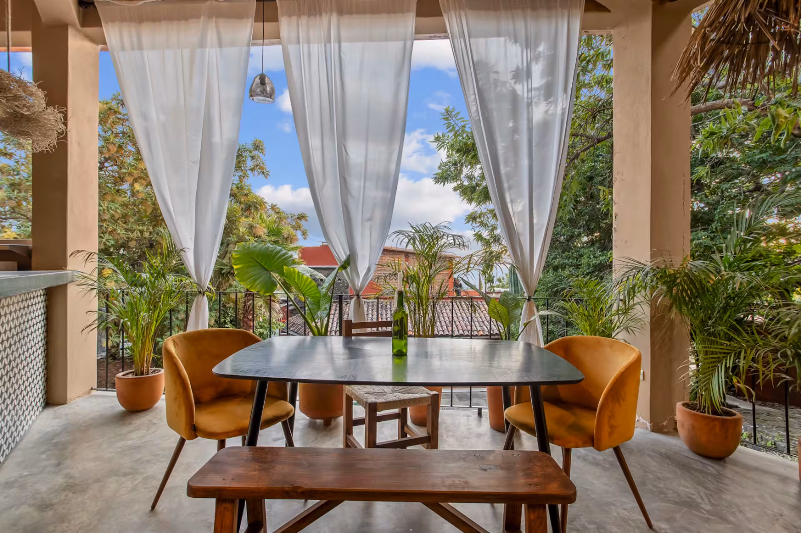 Dining table under a palapa roof with hanging plants above.