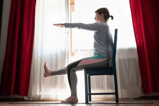 A woman doing the alternate leg raises on a chair to lose weight and burn calories.