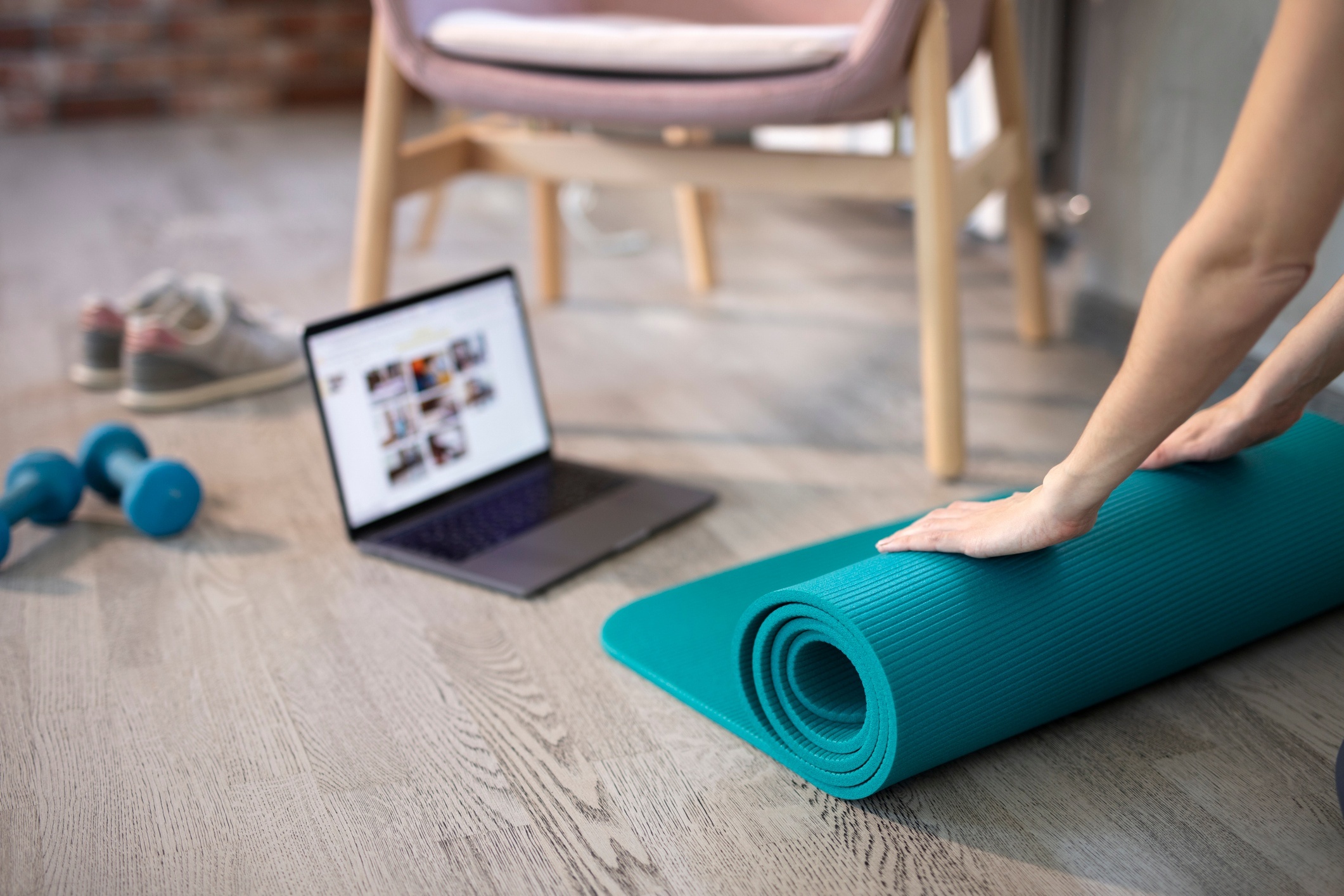 Woman rolling out a yoga mat to prepare for her online workout session.