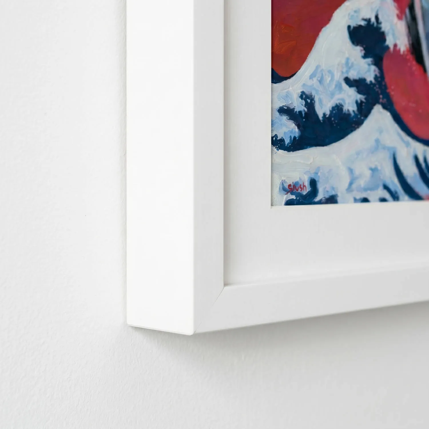 angled view of the edge of a painting's white frame hanging on a white wall