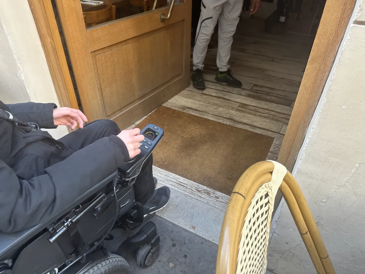 Entrance to Kémia — step-free access from pavement with a wide manual door and wheelchair entering