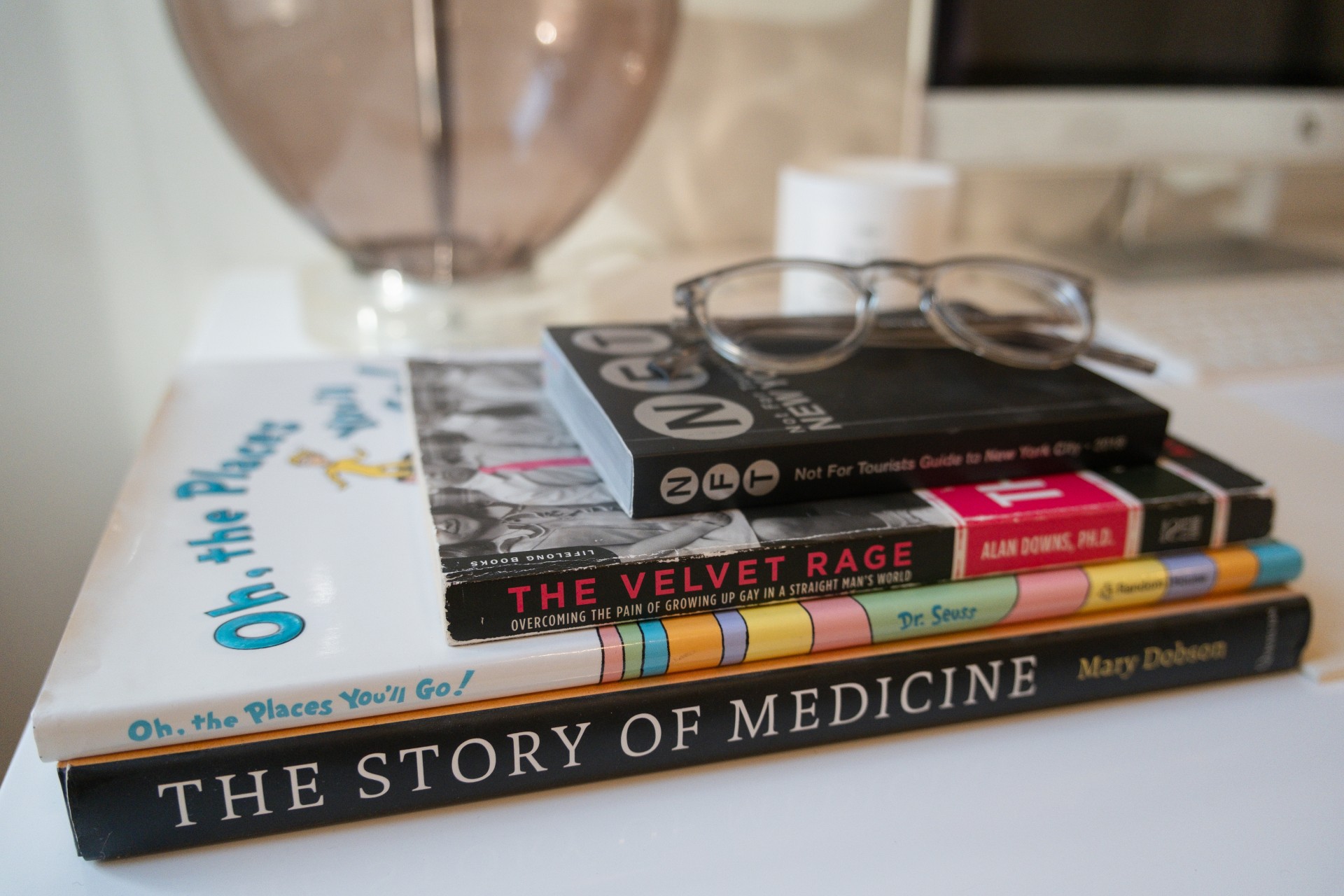 Books stacked atop each other on a table with glasses on the top