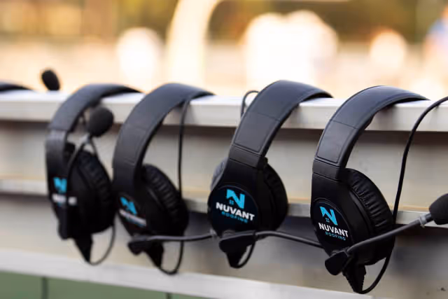 Four black headsets with microphones hanging in a row on a white rail, each labeled with the Nuvant logo.