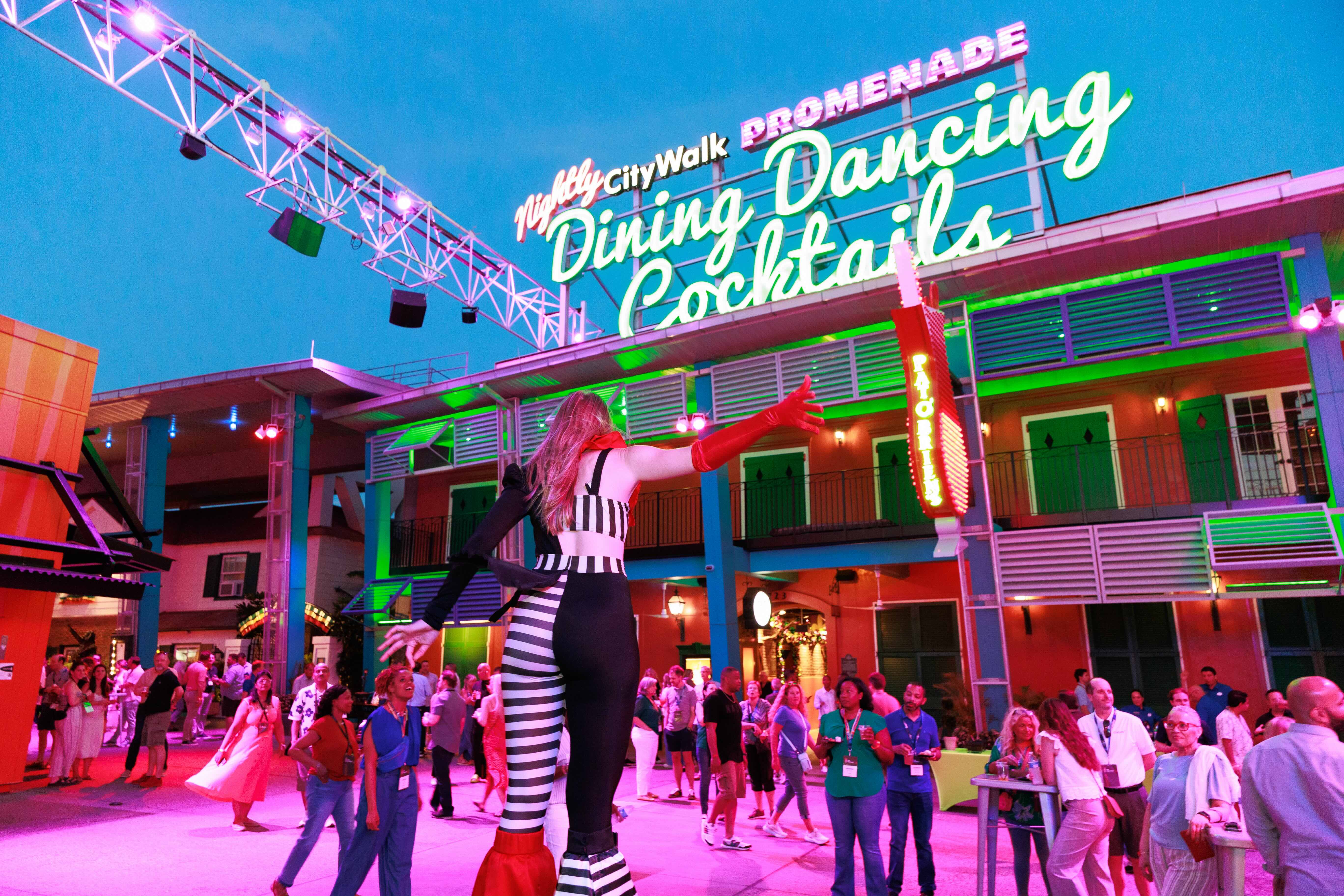 A woman dressed up on stilts facing an audience on the promenade