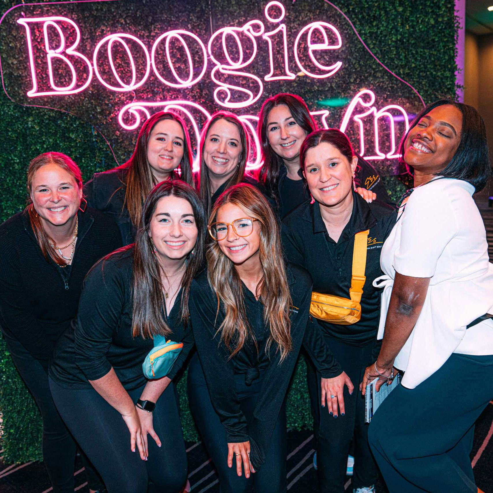 A group of young people posing at an event in front of a greenery wall with fluorescent signage that says "Boogie".