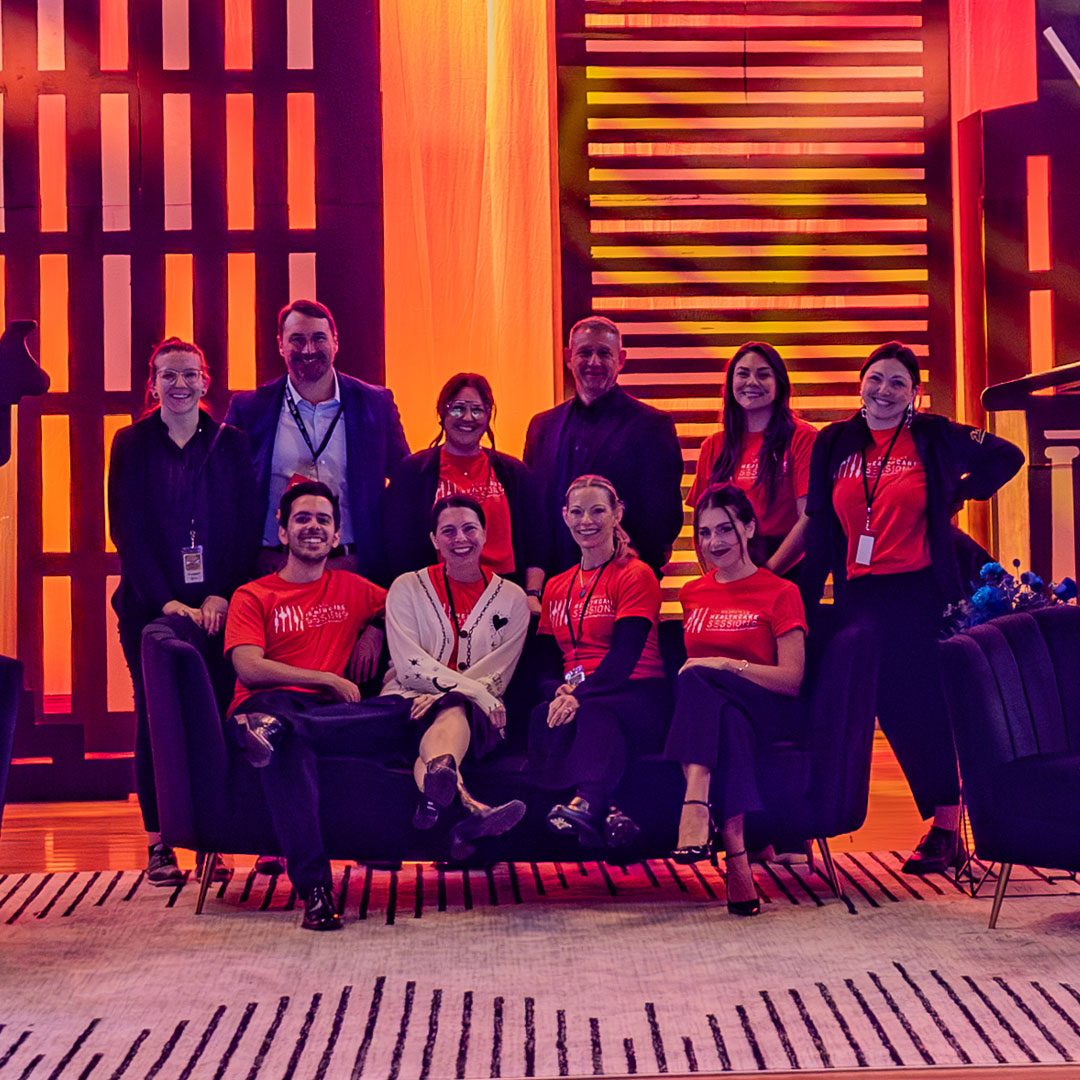 Group of men and women with badges around their necks, in front of a wall of lights.