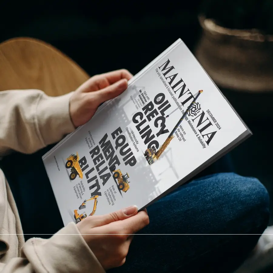 Person holding and reading a magazine titled 'MAINTENANCE' with cover topics about oil recycling and equipment reliability, featuring illustrations of construction vehicles.