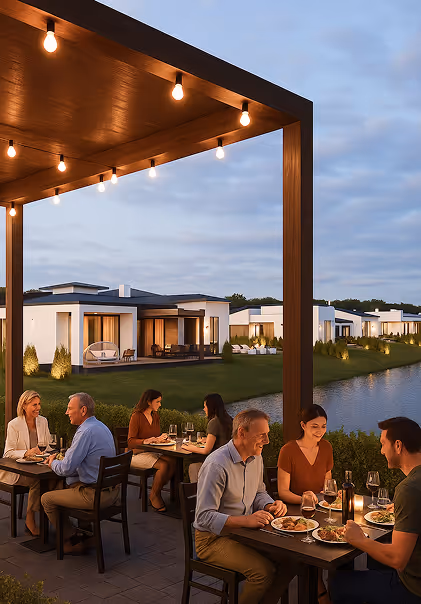 Люди вечеряють на терасі біля води з видом на сучасні котеджі, увечері при світлі ламп