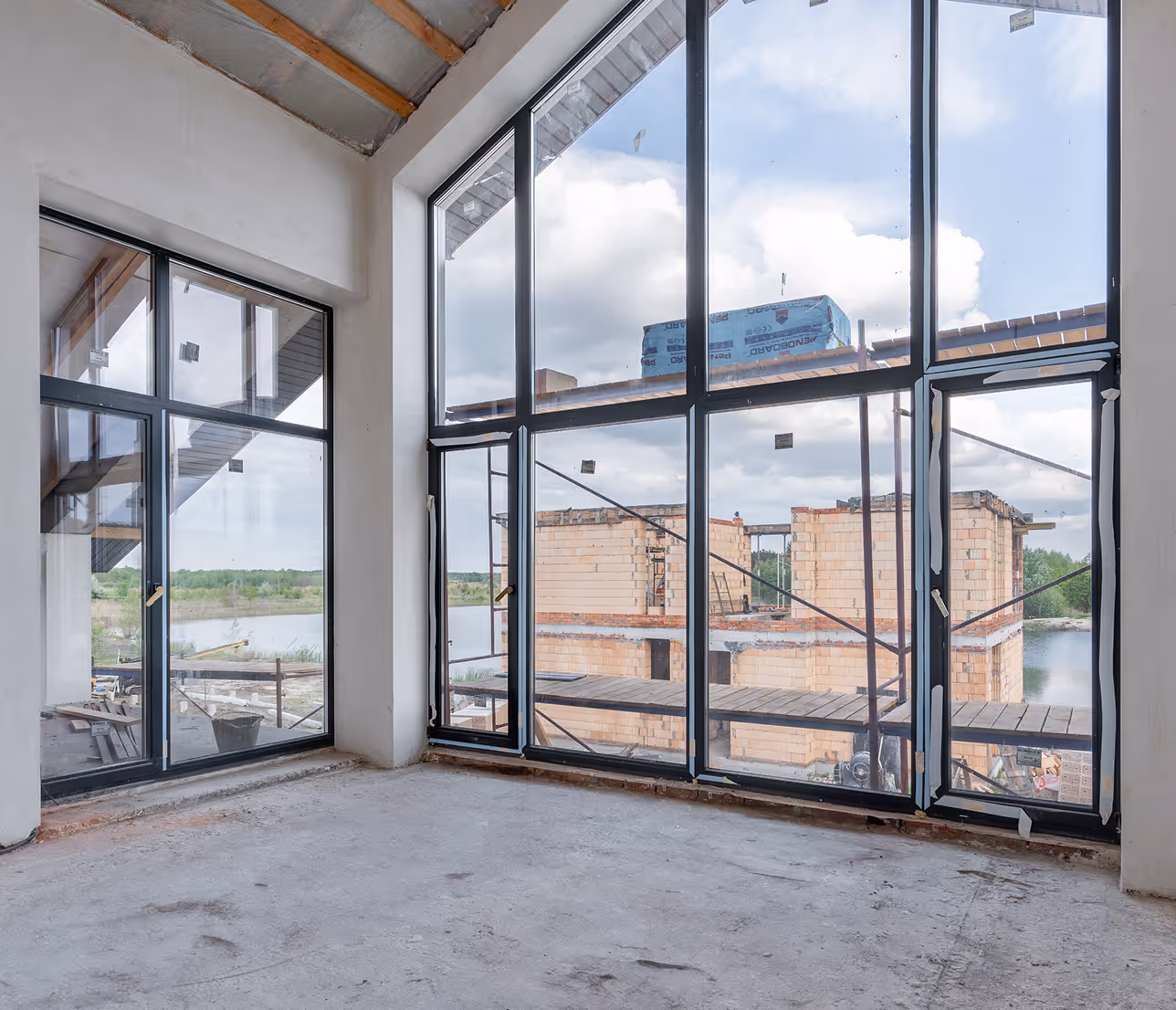 Інтер’єр будинку на етапі будівництва з великими панорамними вікнами та видом на водойму і сусідні будівлі