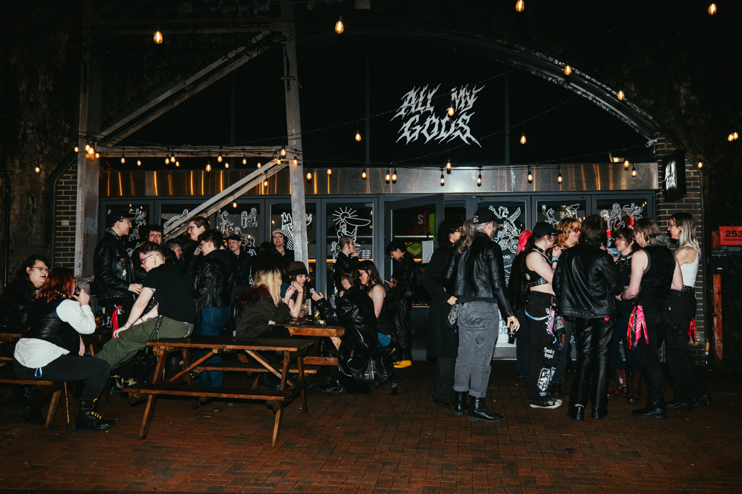 Group of people wearing dark clothes gathered outside a venue named All My Souls at night.