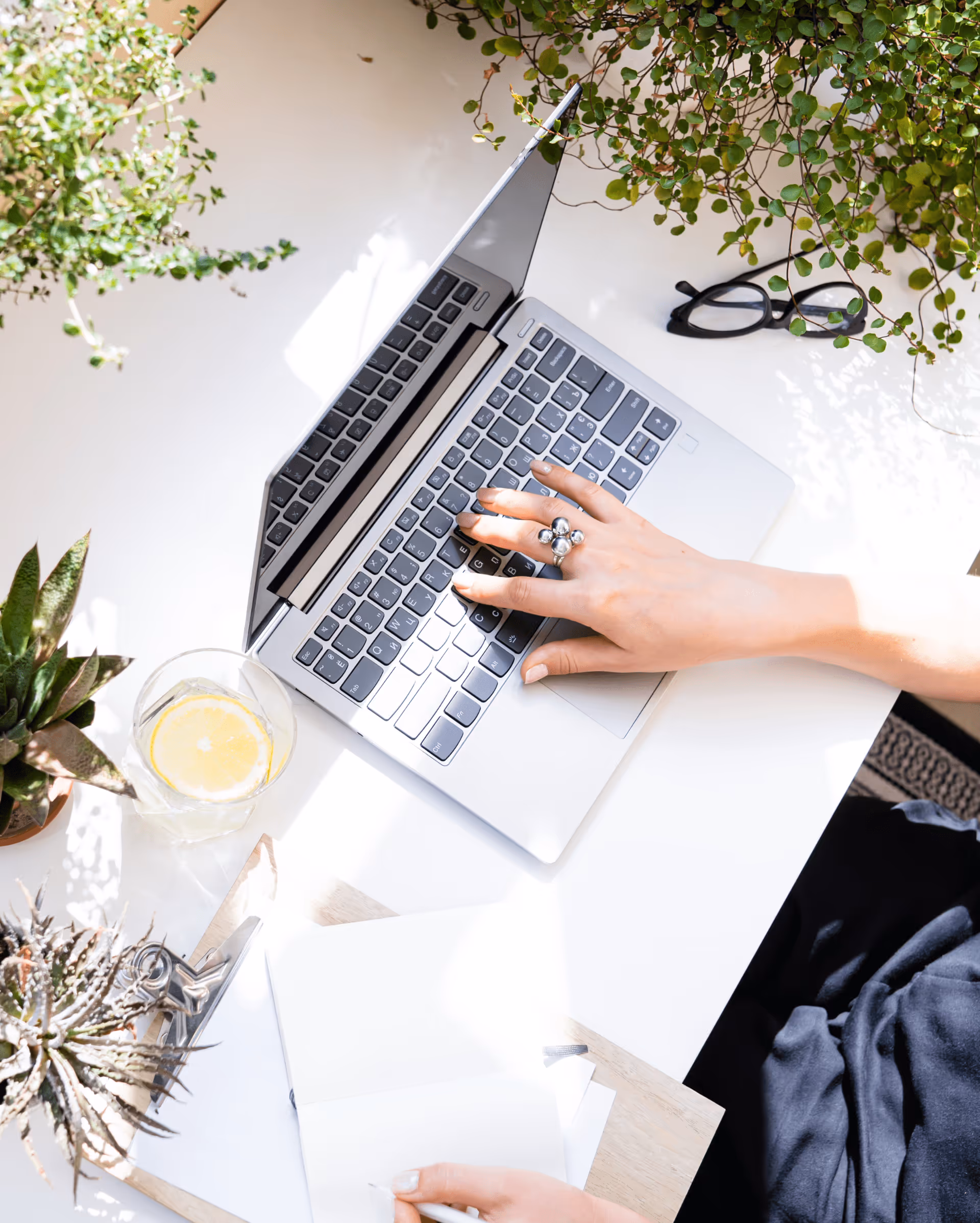 A woman working on a laptop surrounded by plants. 