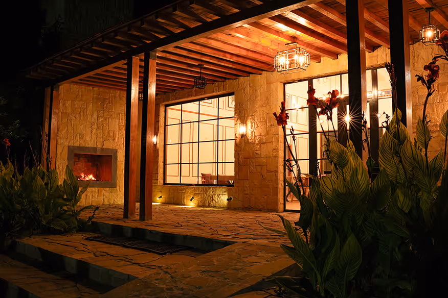 The beautifully illuminated main building at Angirasa resort at night, featuring a stone facade, a cozy outdoor fireplace, and a warm, inviting ambiance for guests near Hyderabad.