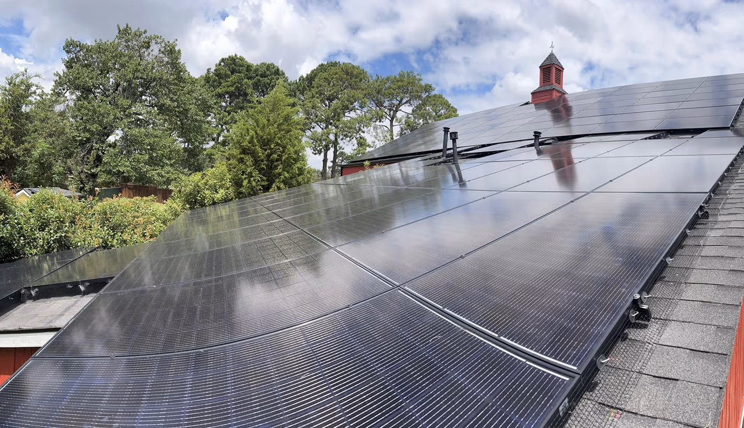 Close-up of solar panels installed on a residential roof with trees and a blue sky with clouds in the background.