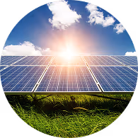 Solar panels installed on grassy ground with the sun shining brightly and a partly cloudy blue sky.