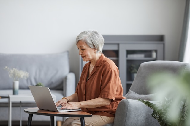 Older woman in brown shirt working on laptop in minimalist living room