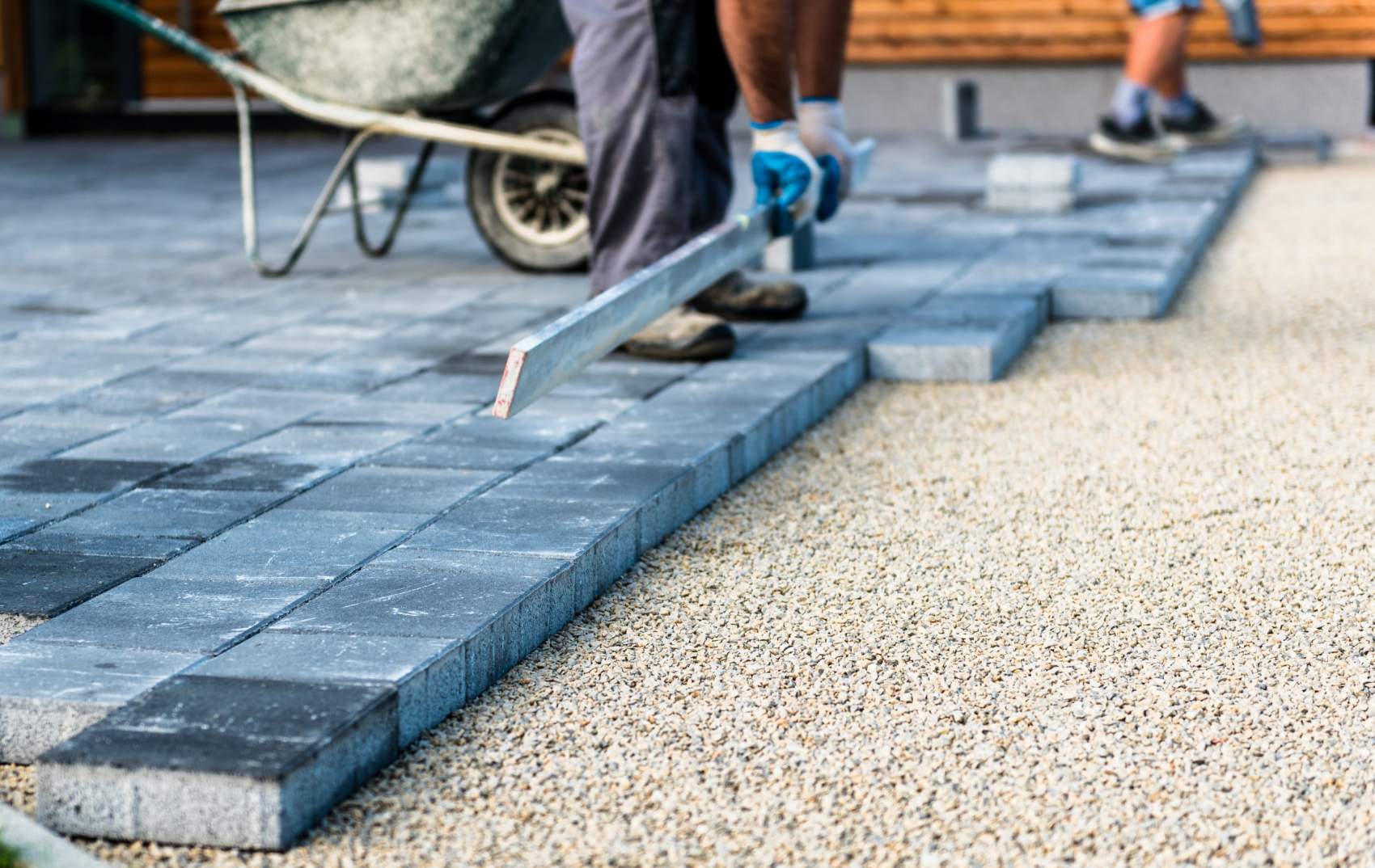 Laying gray concrete paving slabs in house courtyard driveway patio. Professional workers bricklayers are installing new tiles or slabs for driveway, sidewalk or patio on leveled foundation base made of sand at public or private residence.
