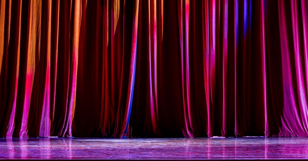 Une scène avec un rideau et un projecteur allumé, prête pour une performance.