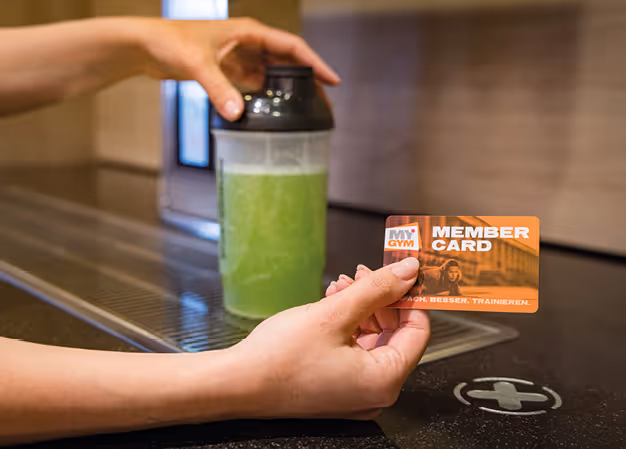 Jemand hält eine Mitgliedskarte von MY GYM in einer Hand und einen grünen Shake in einem Fitness-Shaker in der anderen Hand.