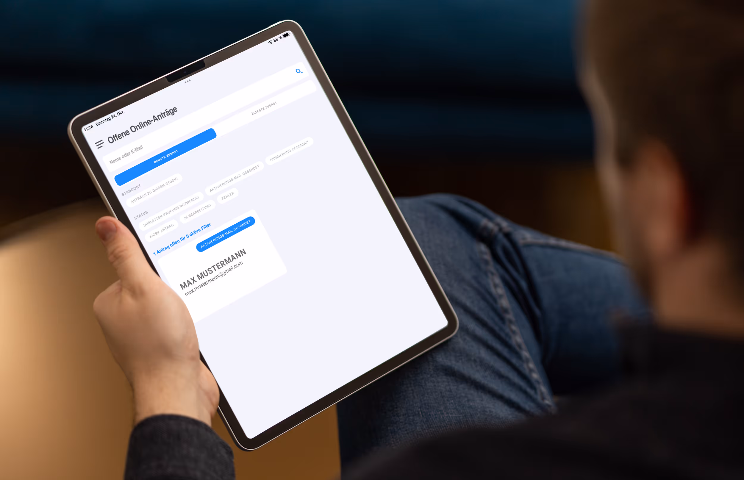 Ein Mann hält ein Tablet, das eine deutsche Benutzeroberfläche mit offenen Online-Anträgen anzeigt.