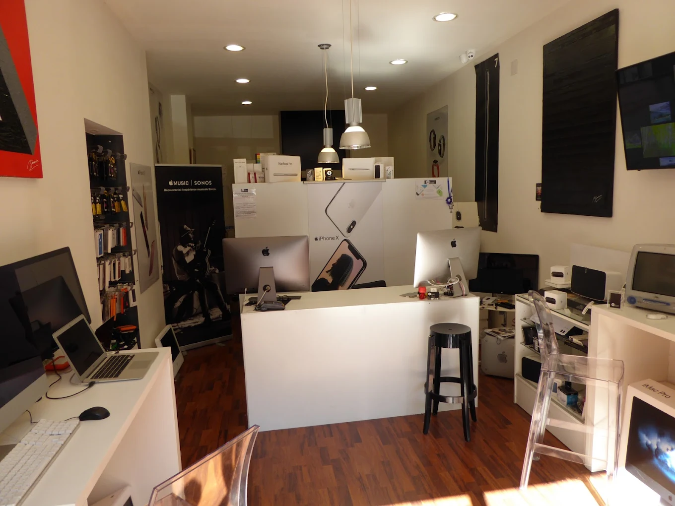 Interior of an Apple product store with desks, iMacs, MacBook Pro, iPhone X poster, and various accessories.
