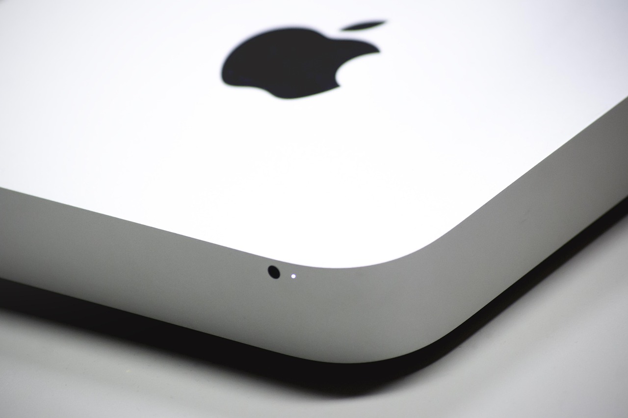 Close-up of a white Apple device corner showing the black Apple logo and a small light indicator on a gray surface.