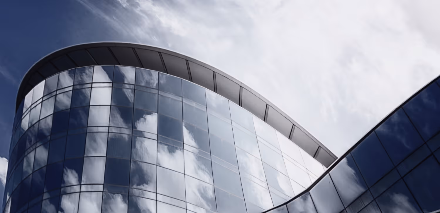 A tall building covered with glass windows, reflecting the clouds and sky.