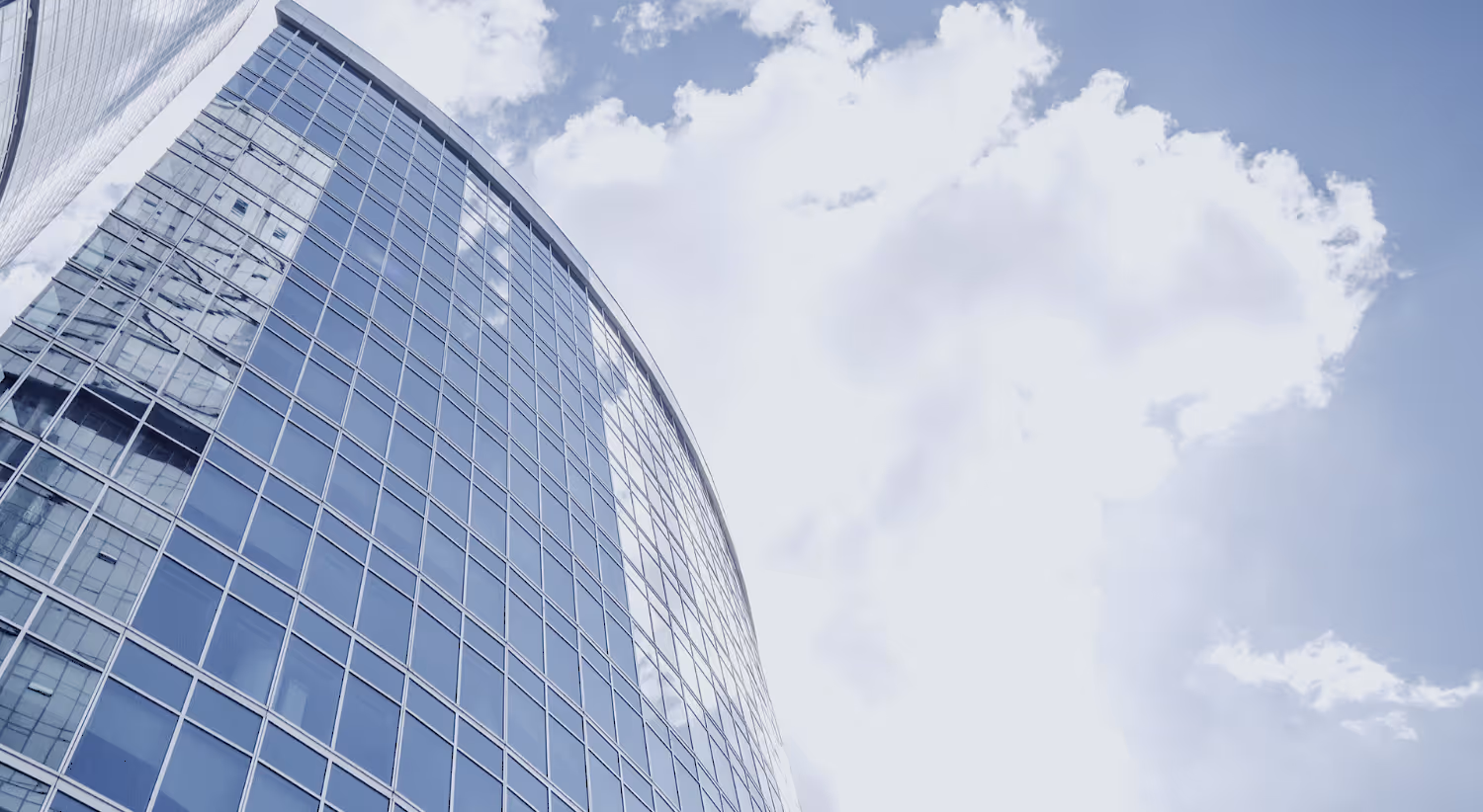 High rise building made of glass reflects sunlight and cloudy sky.