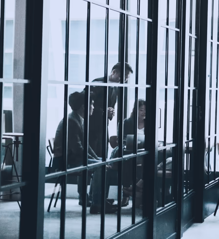 Reflection in glass of a group of professionally dressed people looking at a computer screen. 