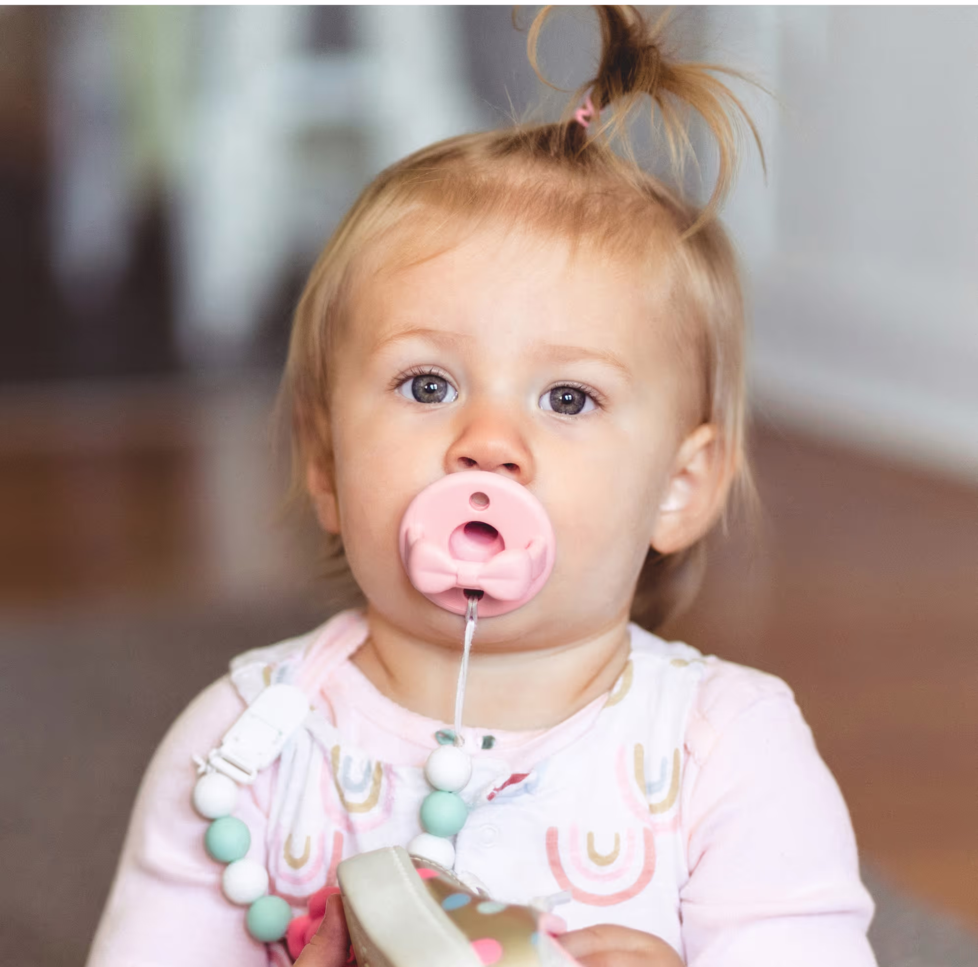 Ein Baby Mädchen mit einem rosa Schnuller im Mund.