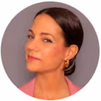 Portrait of a woman with dark hair pulled back, wearing gold hoop earrings and a pink top, against a gray background.