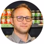 Man with glasses and short hair standing in front of shelves with colorful canned drinks.