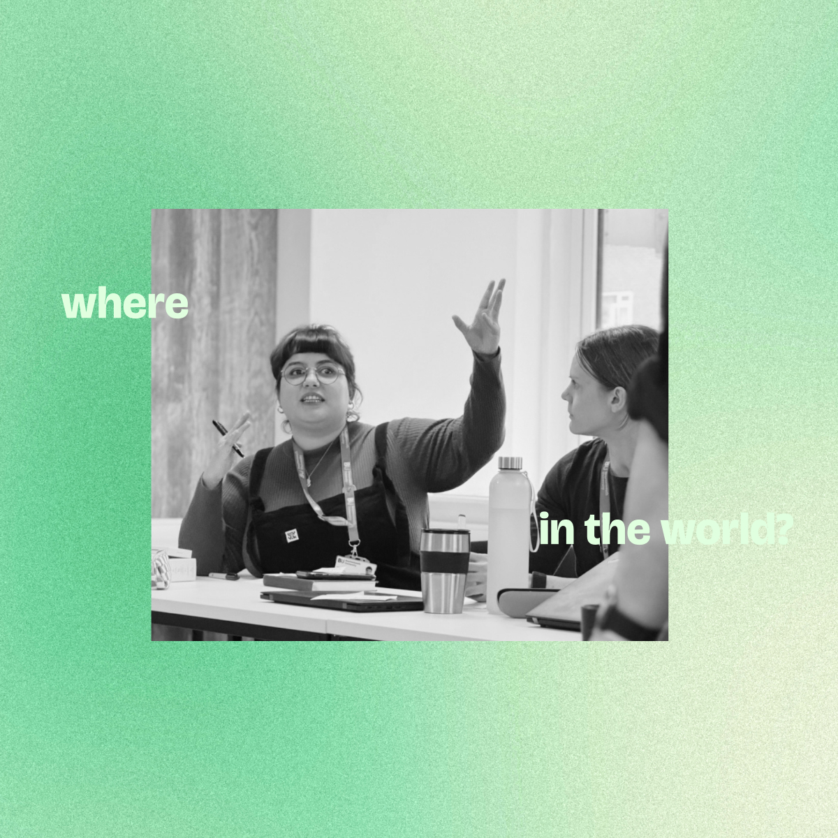 Two women seated at a table engaged in conversation during a meeting, one gesturing with her hand while holding a pen.