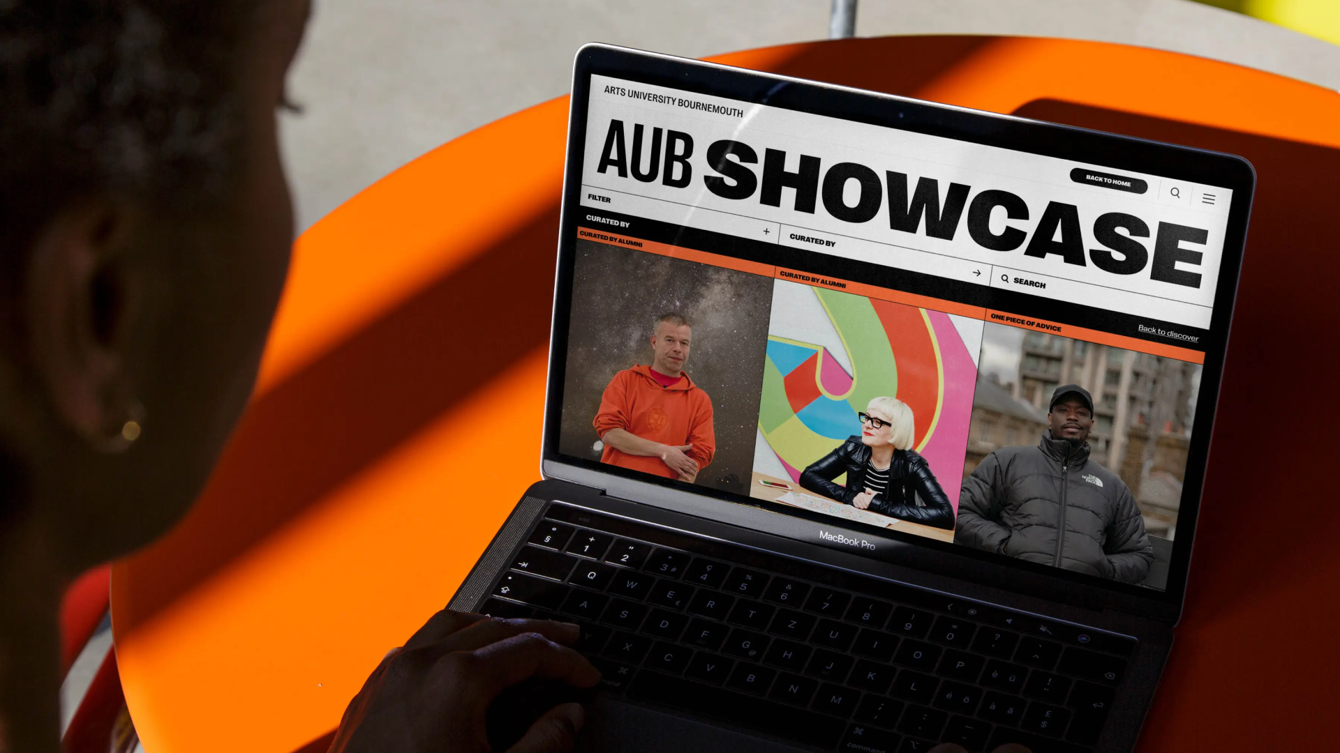 Person viewing the Arts University Bournemouth AUB Showcase website on a MacBook Pro with portraits of three individuals displayed.