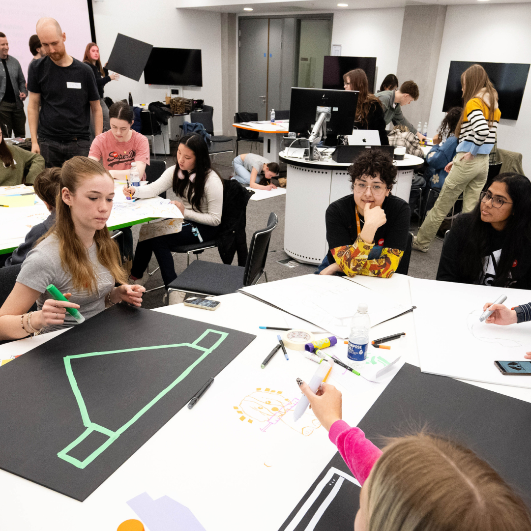 Group of young people engaged in drawing and creative activities around tables in a workshop room.