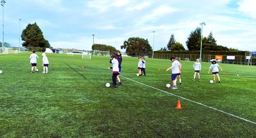 Picture of children playing football with audible balls while a coach supports them