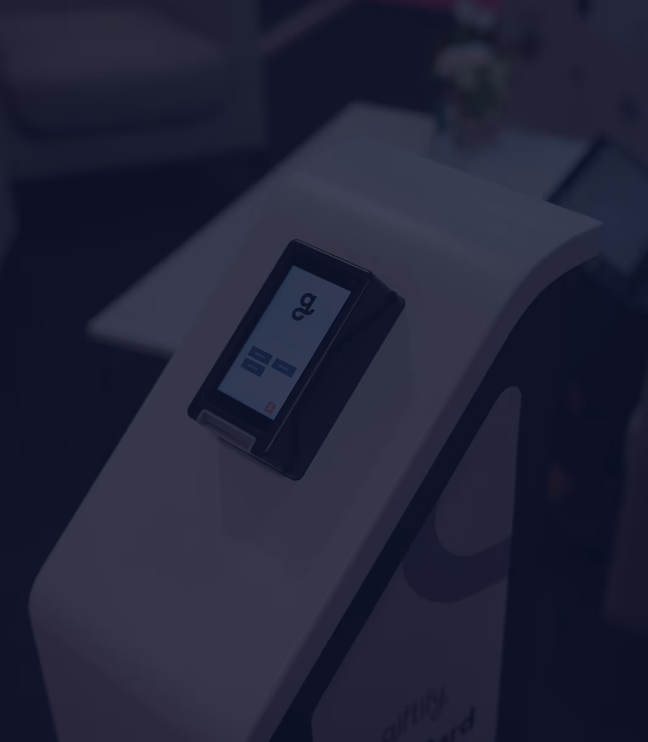 A dimly lit, close-up shot of a white Giftify kiosk with a black screen showing the logo and a login interface. The logo is also visible on the base of the kiosk.
