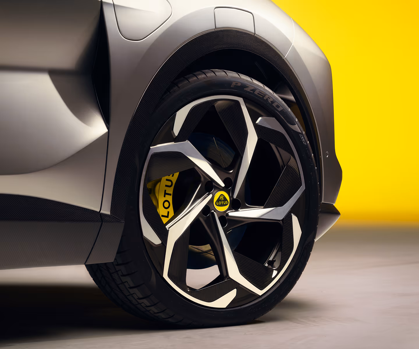 Close-up of a modern car wheel with a Lotus logo on the yellow brake caliper and a yellow background.