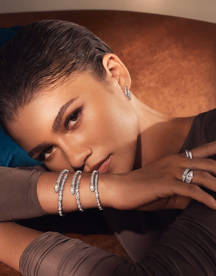 Woman resting her head on her arm, wearing multiple diamond bracelets, earrings, and rings.