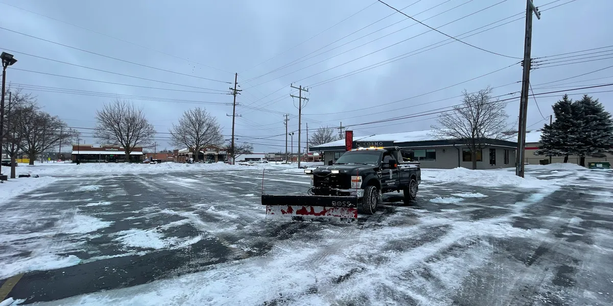Jake's Lawn Care snow removal and plowing service truck clearing commercial parking lot in Michigan winter