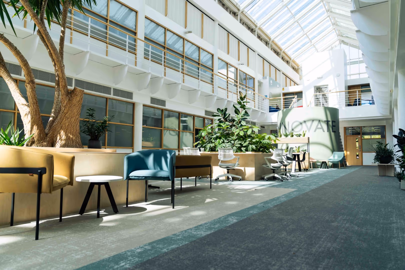 Bright, modern atrium with skylights, indoor plants, and a mix of lounge and workspace seating.