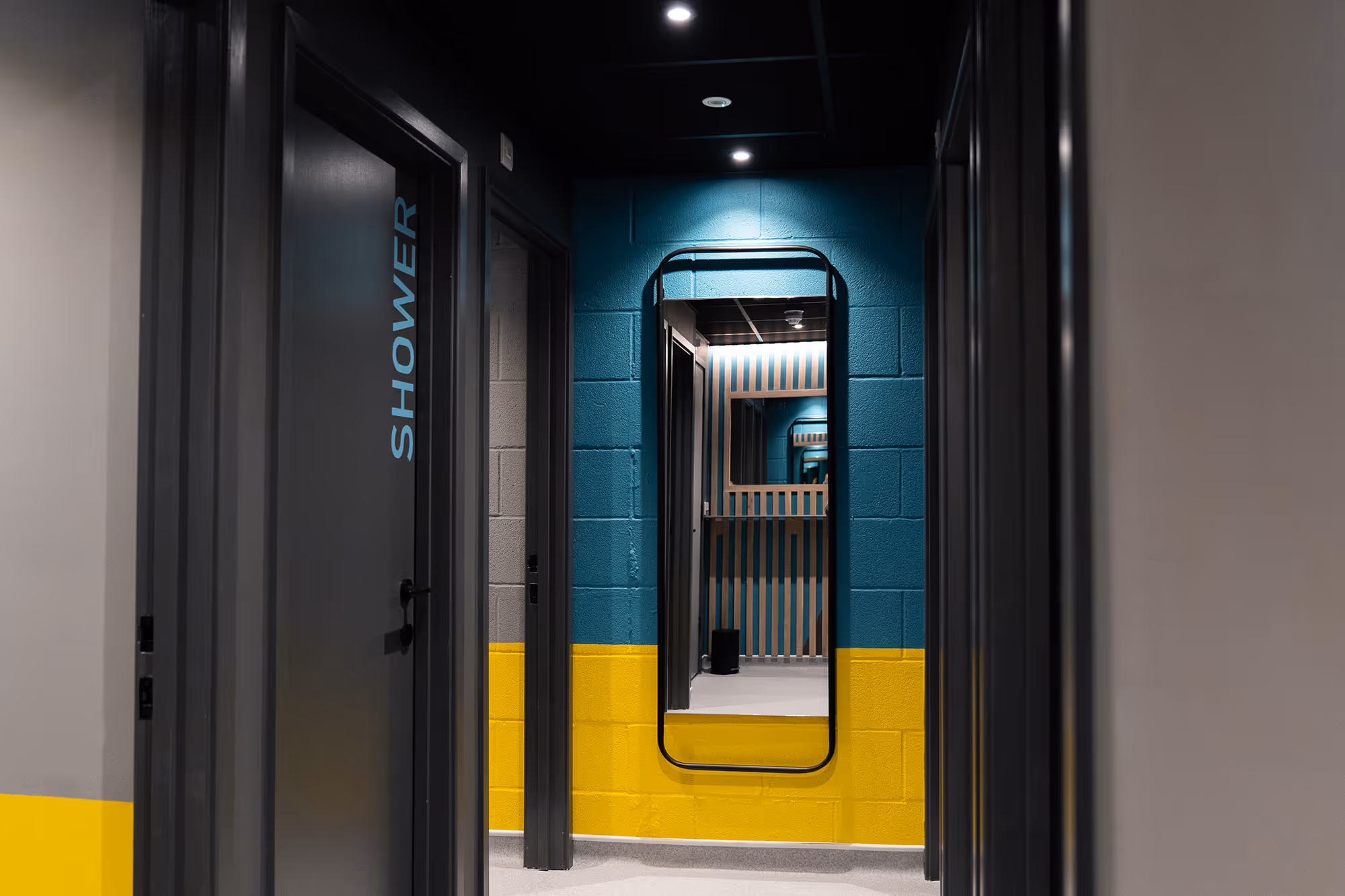 Modern hallway with bold teal and yellow walls, featuring a large mirror and grey shower room doors.