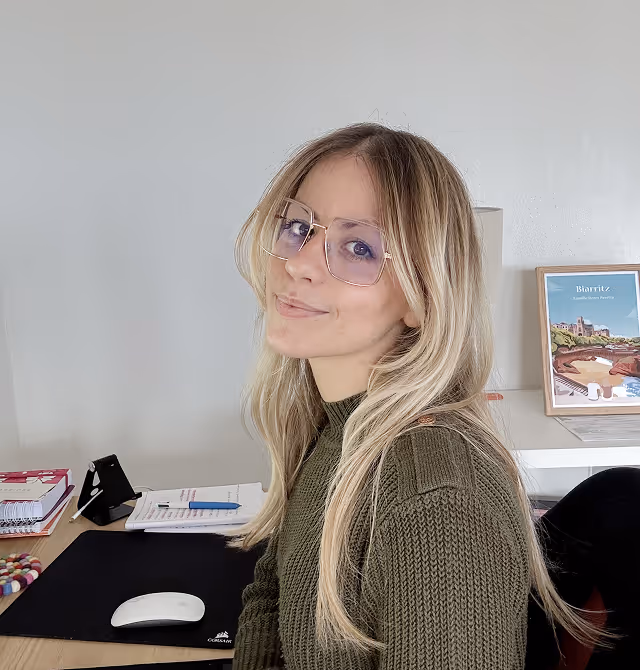 Lara qui regarde l'objectif pendant qu'elle travaille sur son bureau