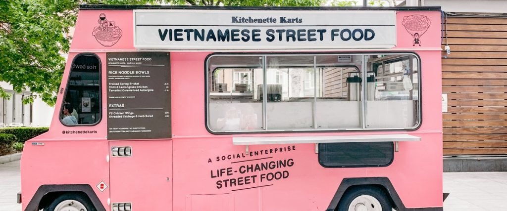 a pink food truck with the words 'Vietnamese Street Food' parked in front of an office building