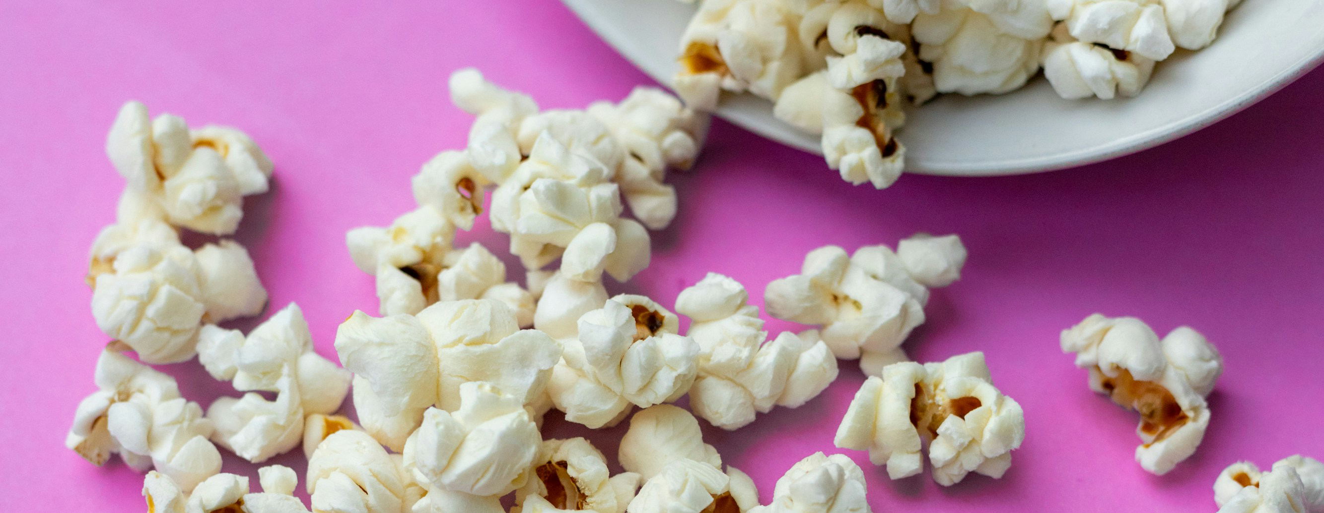 Popcorn spilling off of a plate on a pink background.