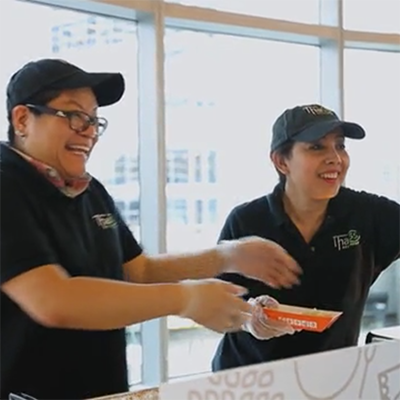 Two smiling Asian women handing over plates at a Fooda event