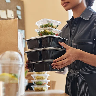 woman holding a stack of packaged restaurant meals.