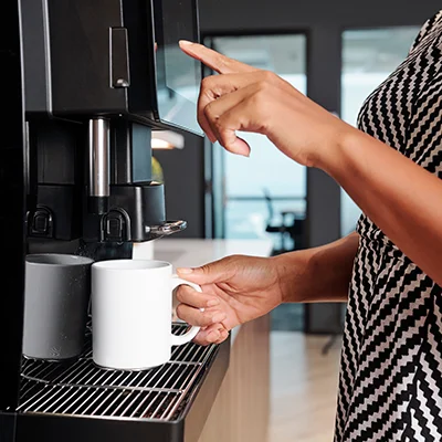 woman's hands put a coffee cup under an automatic coffee maker while tapping the touchscreen.
