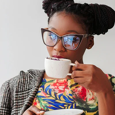 Beautiful Black woman in glasses sips coffee from a demitasse cup.
