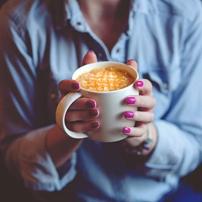 Focus on a woman's hands holding a cup of coffee with a caramel drizzle on top.