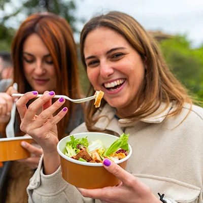two college girls eat mediterranean salad bowls outside.